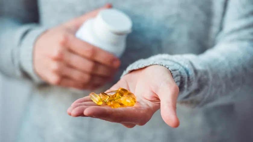 A woman holding several fish oil supplement pills in the palm of her outstretched hand